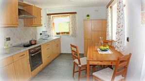 Een keuken met houten kastjes, een fornuis en een eettafel met stoelen.