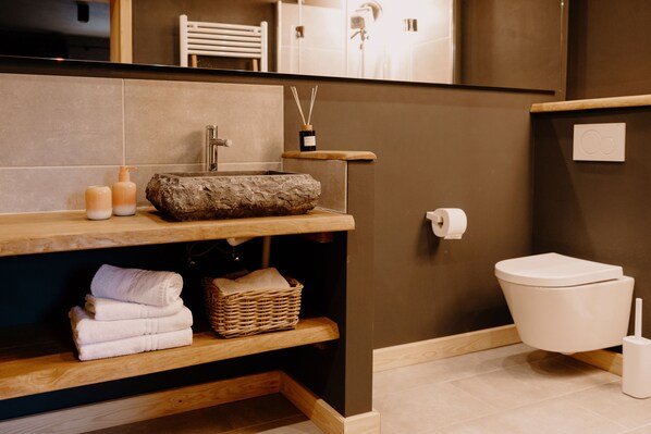 Ein modernes Badezimmer mit einem Steintonne, Holzregalen, einer Toilette und einem Spiegel.