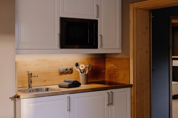 A kitchen with white cabinets, a stainless steel sink, a microwave, and wooden countertops. - (2) Zwei-Raum-Ferienwohnung 30 qm, Dusche/WC, Küche, Terrasse u. Garten (Reit im Winkl)