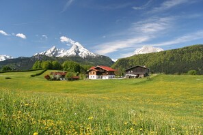 Un paysage rural avec une maison et une grange, entourés de champs verdoyants et de montagnes.
