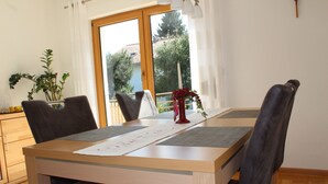 Ein Essbereich mit einem Holztisch, vier Stühlen, einer Vase mit einer roten Blume und einem Fenster mit Blick auf Bäume und ein Gebäude.