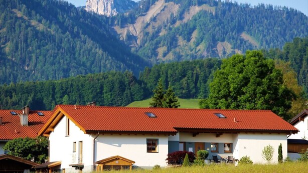 Ein Haus mit rotem Ziegeldach, weißen Wänden und einer Bergkulisse.
