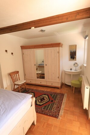 Une chambre avec une armoire en bois, un lit simple, une chaise, un petit bureau, un radiateur et un tableau accroché au mur.