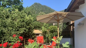 Eine Terrasse mit Tisch und Stühlen, umgeben von roten Blüten und grünem Blattwerk.