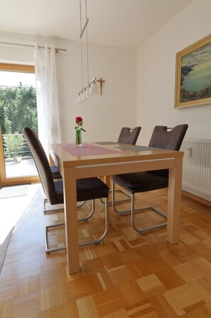 Un coin repas avec une table en bois, quatre chaises, un vase contenant une fleur rouge et un tableau accroché au mur.