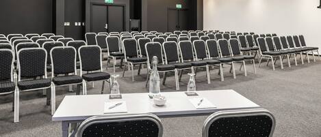 A conference room with rows of chairs, tables, and a projector screen.