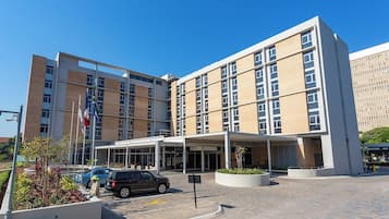 A modern building with a covered entrance, a parking area, and a flagpole with multiple flags.