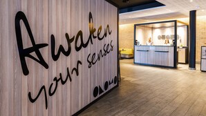 A reception area with a wooden wall displaying the text "Awaken your senses" and a reception desk with a modern design. - ONOMO Hotel Durban (Durban)
