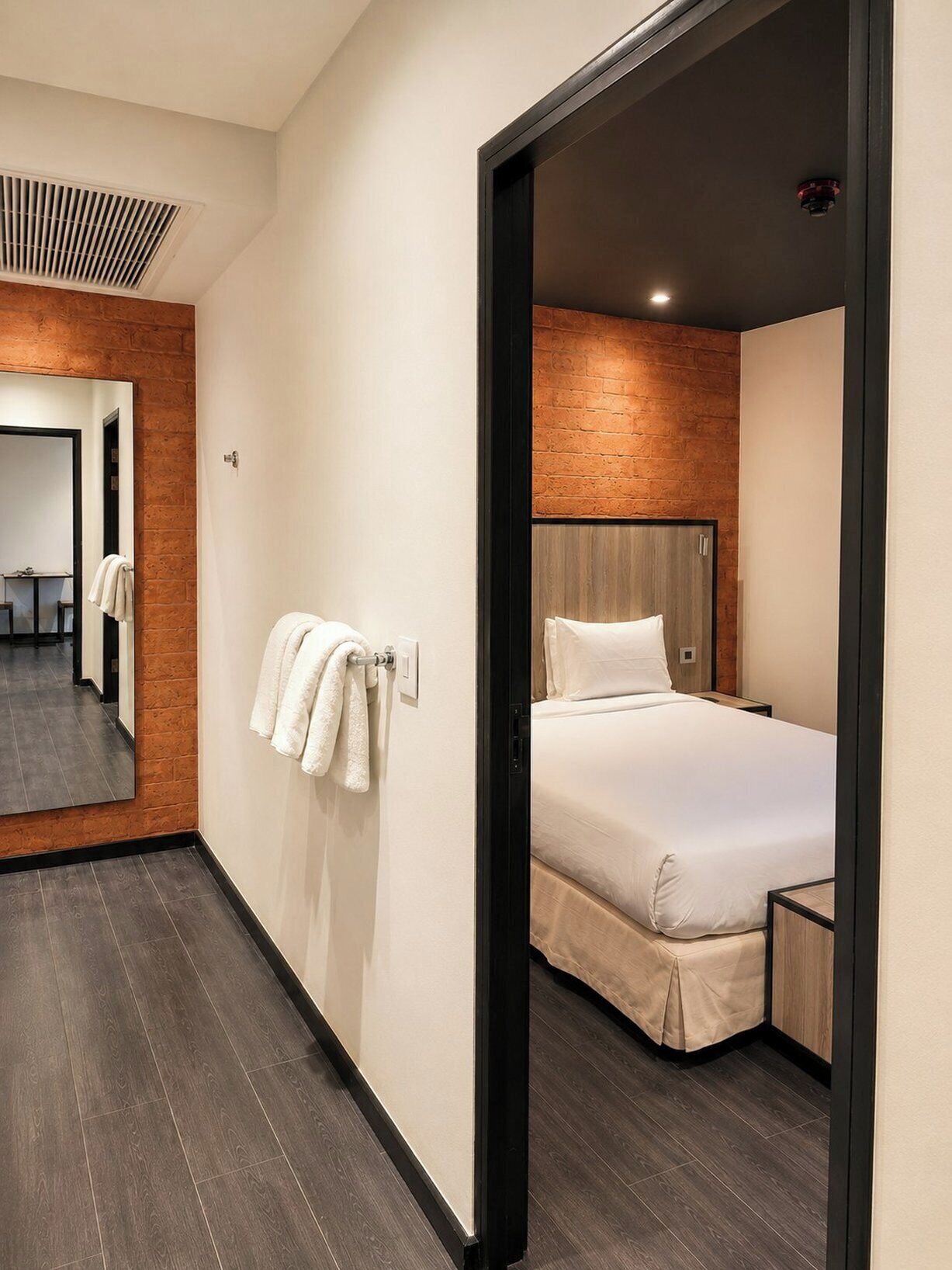 Quarto de hotel moderno com uma cama grande, cabeceira de madeira, um espelho e um porta-toalhas.