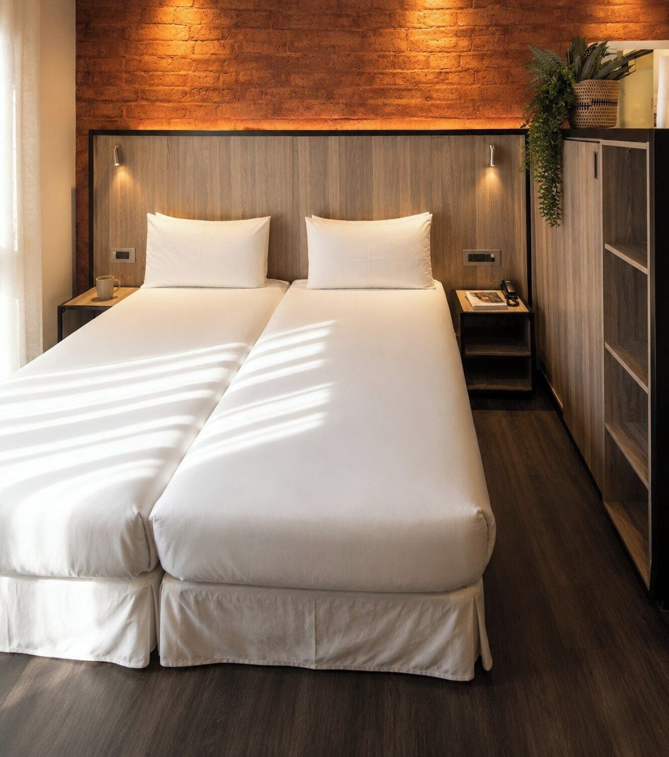 A double bed with a wooden headboard and nightstands, a small table with a lamp, and a plant on a cabinet.