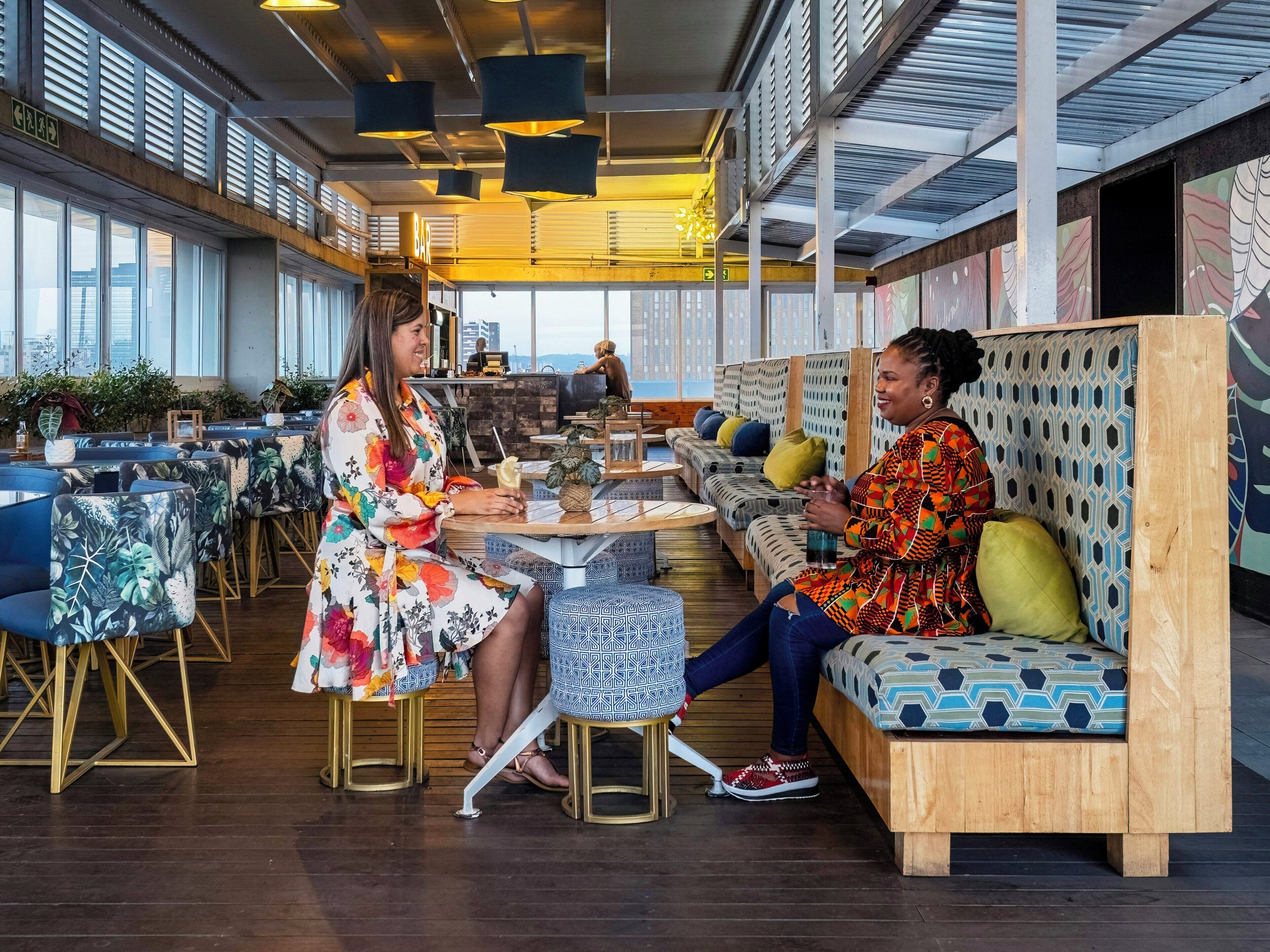 Un área de estar moderna con mesas y sillas, un bar y vistas a la ciudad.