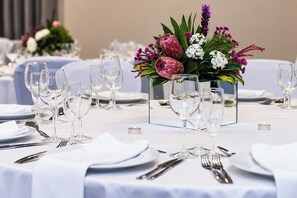 Une table à manger dressée avec de nombreux verres à vin, des assiettes et des couverts, agrémentée d’un centre de table composé de fleurs et de bougies.