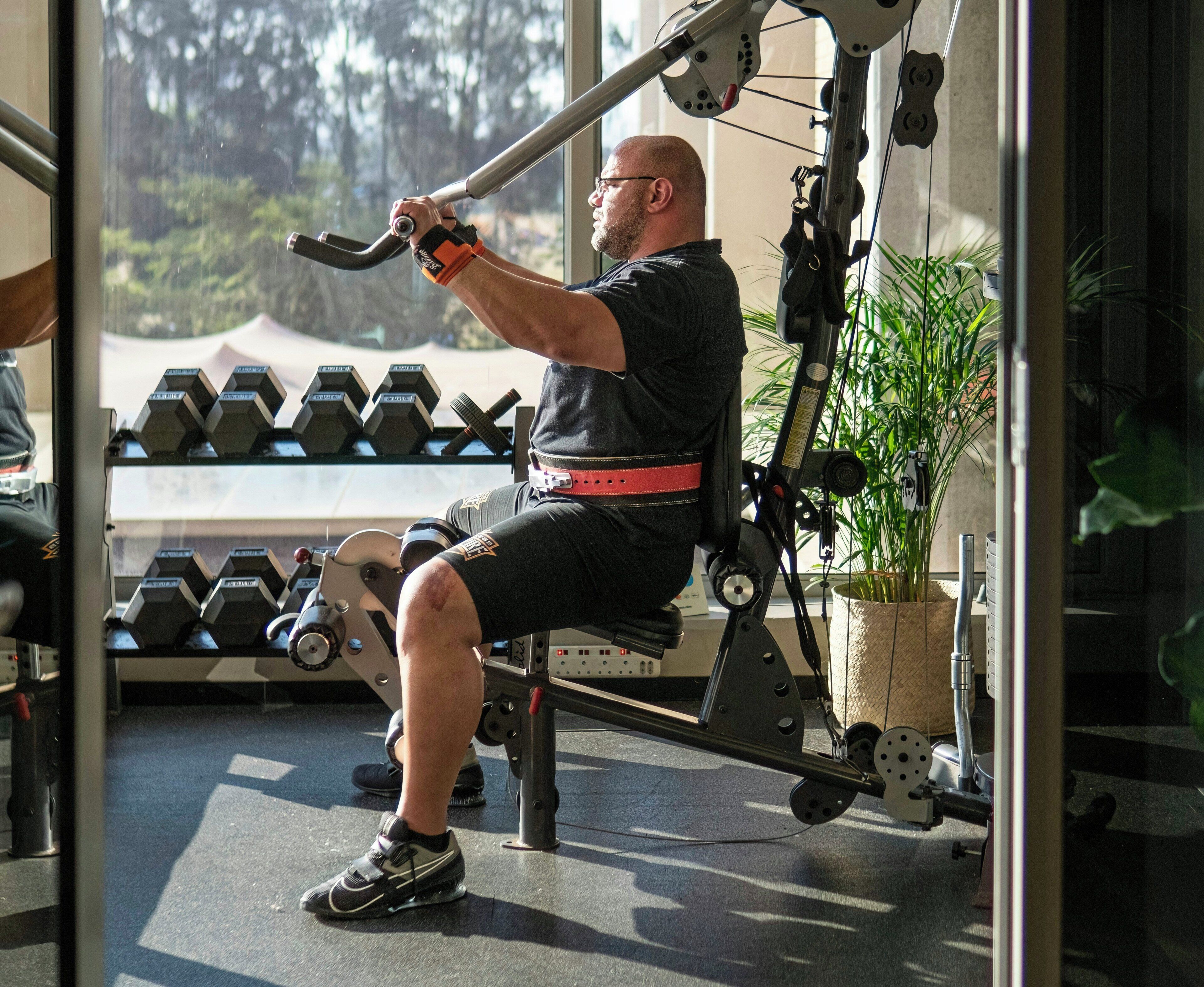 A man using a leg press machine in a gym with dumbbells and a plant in the background.