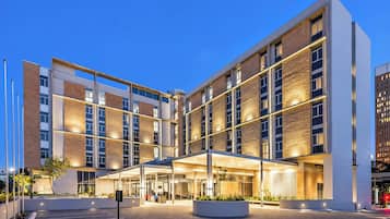 Um hotel moderno com fachada de vidro, vários andares e área de entrada coberta.