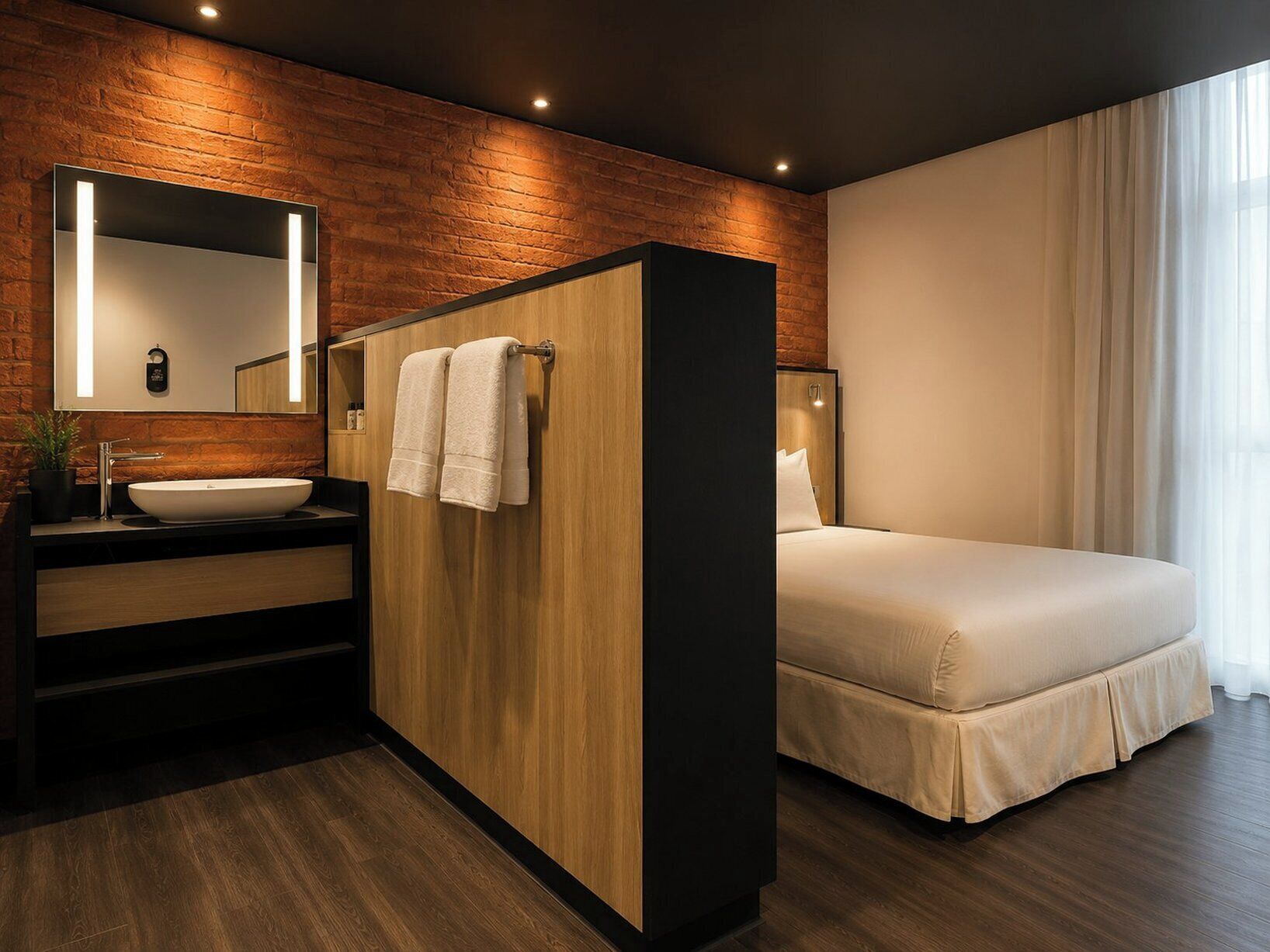 Un baño moderno con un tocador de madera, un espejo grande y una cama con cubrecama blanco.