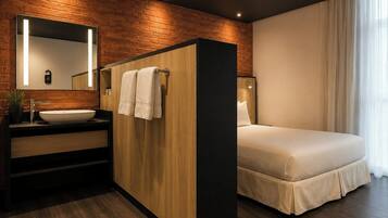 Un baño moderno con un tocador de madera, un espejo grande y una cama con cubrecama blanco.