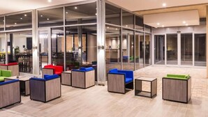 A modern indoor space with glass partitions, multiple seating areas with colorful cushions, and a tiled floor. - ONOMO Hotel Durban (Durban)