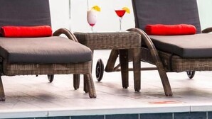 Un espace aménagé au bord de la piscine, comprenant deux chaises longues et une petite table, chacune agrémentée d’un coussin rouge.