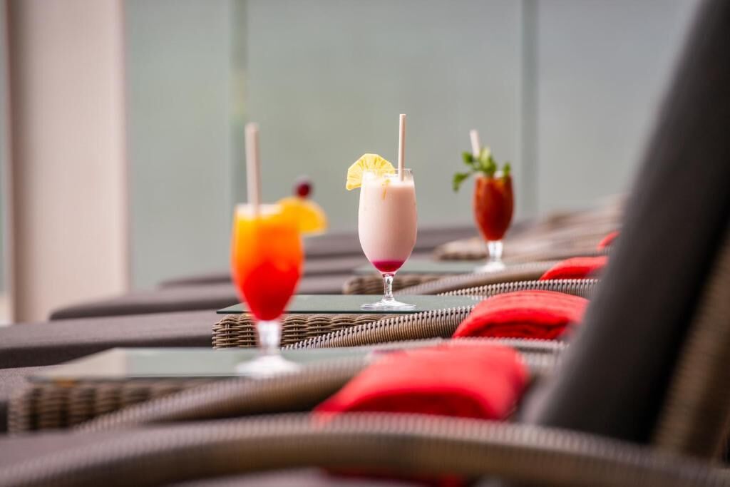 Three drinks on a table with a wicker chair in the foreground.