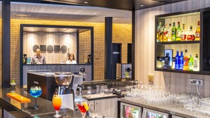 A bar area with a brick wall, a counter with glasses and bottles, and a shelf with various liquor bottles. - ONOMO Hotel Durban (Durban)