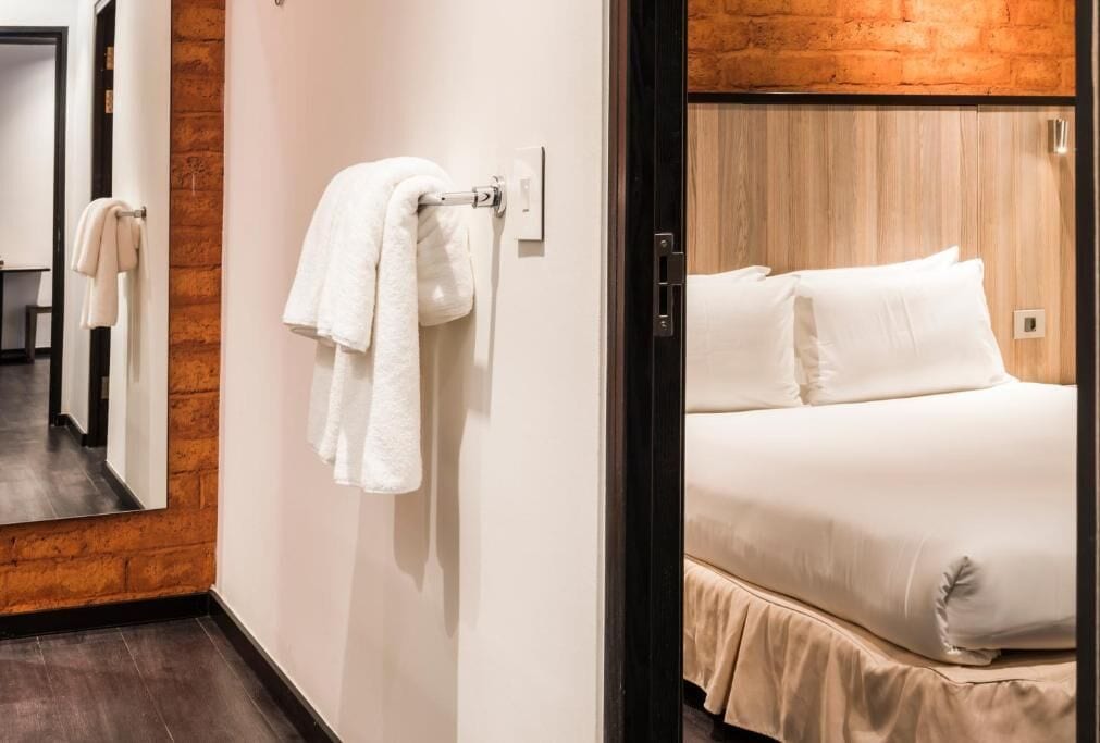 Habitación de hotel con cama, un cabecero de madera y un espejo que refleja el espacio.