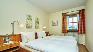 Une chambre d’hôtel avec un grand lit, deux tables de chevet, une commode, une fenêtre avec des rideaux et des œuvres d’art murales.