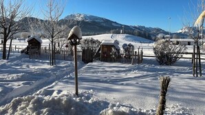 Un paysage enneigé avec une cabane en bois, une zone délimitée par une clôture et une montagne en arrière-plan.