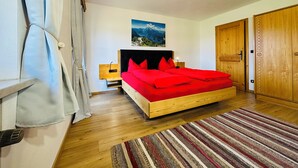Ein Schlafzimmer mit Bett, Nachttisch, Holzschrank, einem Bild an der Wand und einer Deckenleuchte.