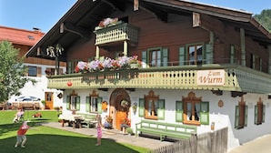 Un edificio de madera tradicional con un balcón decorado con flores, un letrero que dice "Zum Wurm" y un césped bien cuidado.