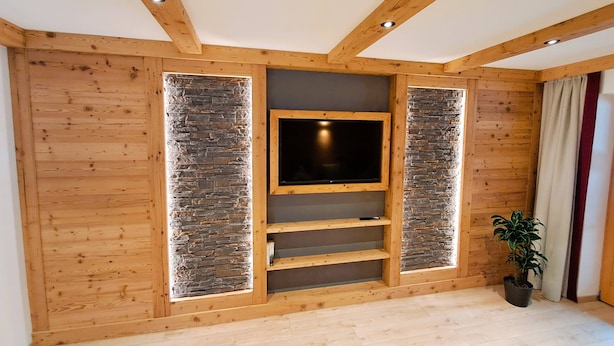 Una habitación con paredes de madera, un detalle de pared de piedra, un televisor de pantalla plana, estantes empotrados y una planta en maceta.