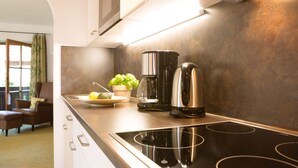 Una cocina moderna con una placa de inducción negra, una cafetera y una planta en maceta sobre la encimera.