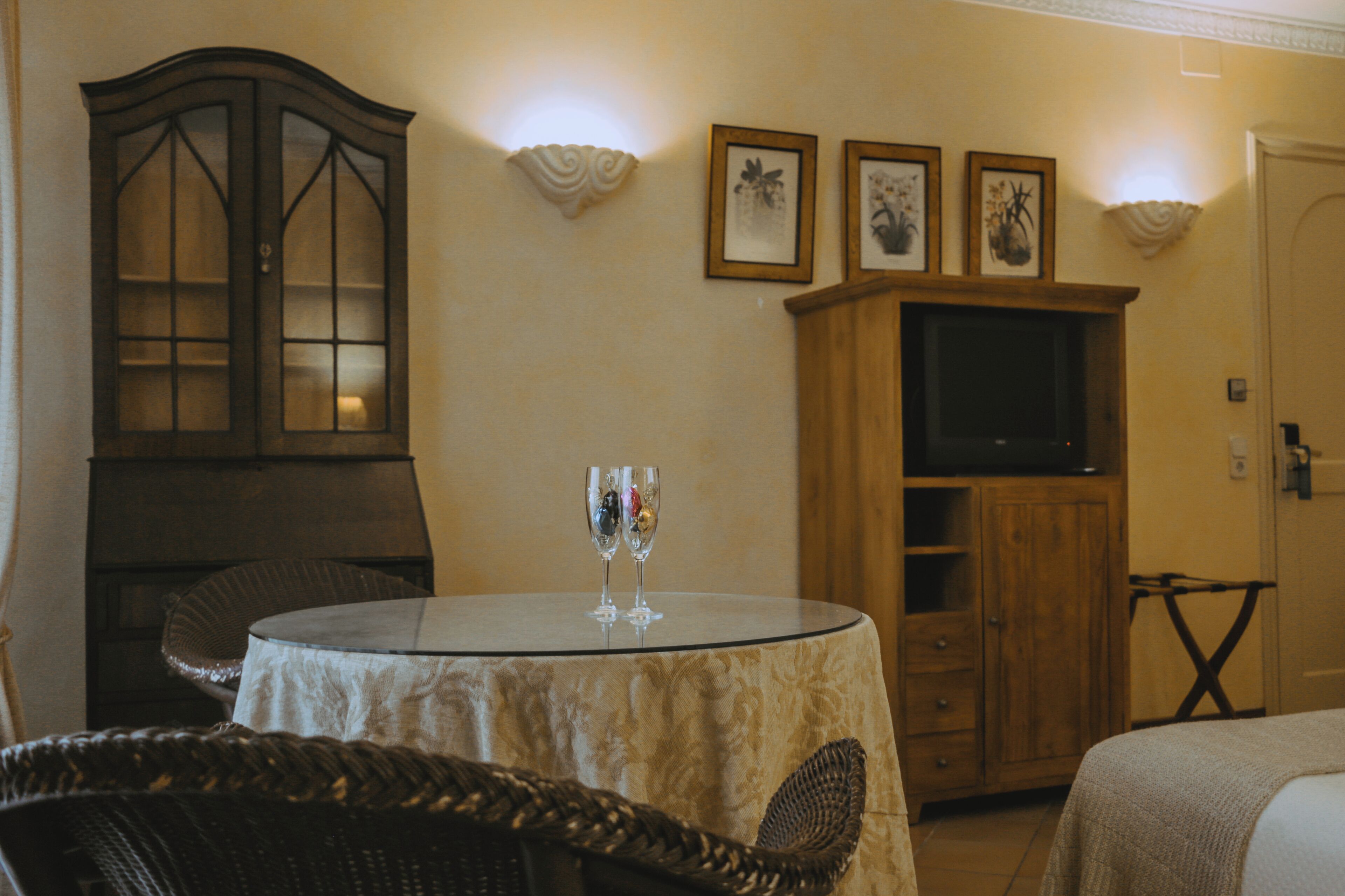 Habitación de hotel con una mesa redonda, sillas de mimbre, un armario de madera y un televisor.