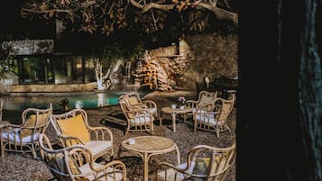 Un espacio al aire libre con sillas y mesas de mimbre, un muro de piedra y una piscina.