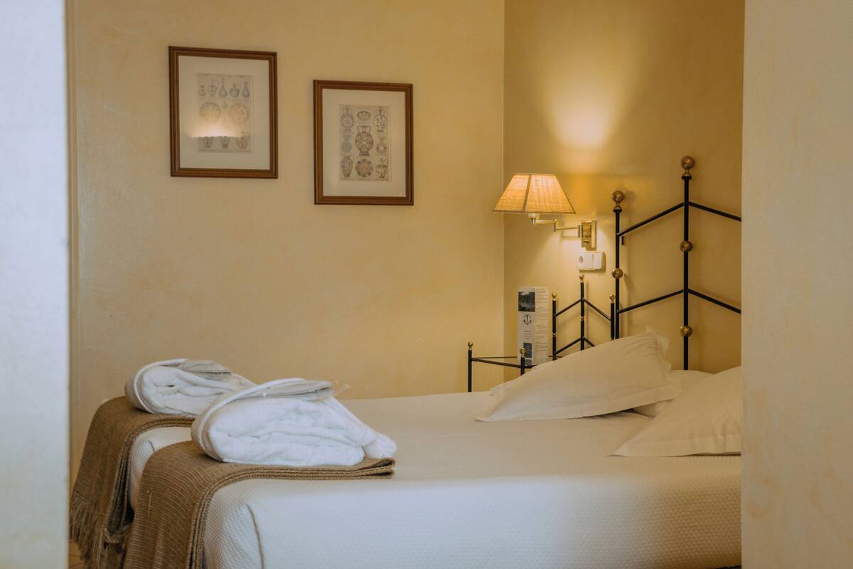 Ein Hotelzimmer mit einem Bett, zwei gerahmten Bildern an der Wand, einer Lampe und Handtüchern auf dem Bett.