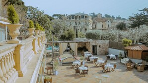 Una terraza con mobiliario exterior, piscina y vistas a edificios históricos.