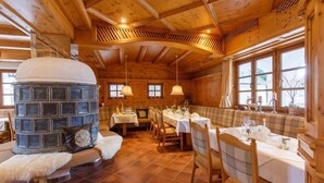 A cozy wooden interior with a stone fireplace, dining tables set for a meal, and large windows allowing natural light. - Family room 30 to 40 sqm, sep. Children's bedroom, fridge, shower, WC (Ruhpolding)