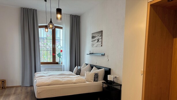 Et soveværelse med seng, sengebord, lampe, vindue med gardiner og et billede på væggen.