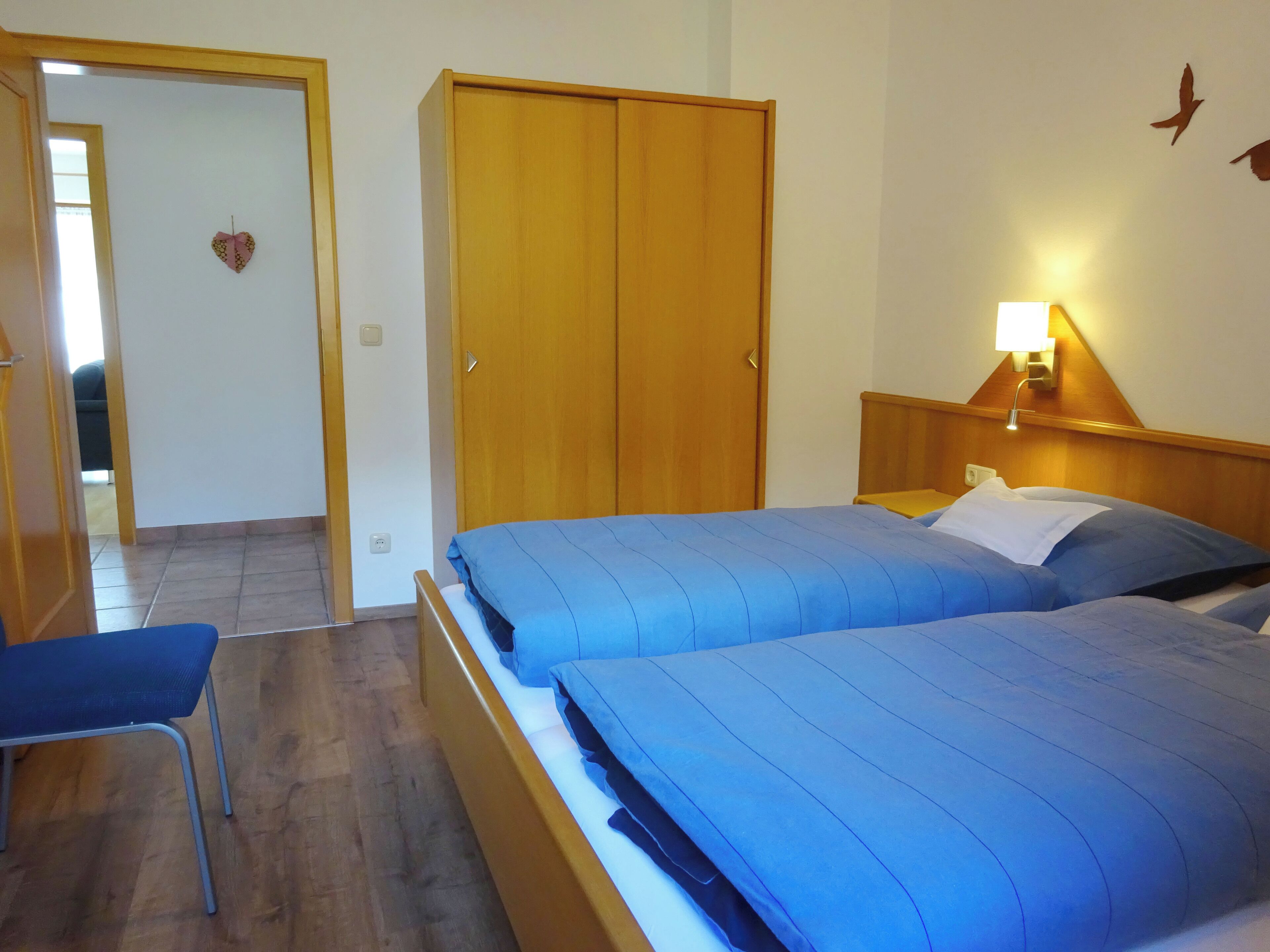 Una habitación de hotel con dos camas, un armario de madera, un escritorio con lámpara y una silla.
