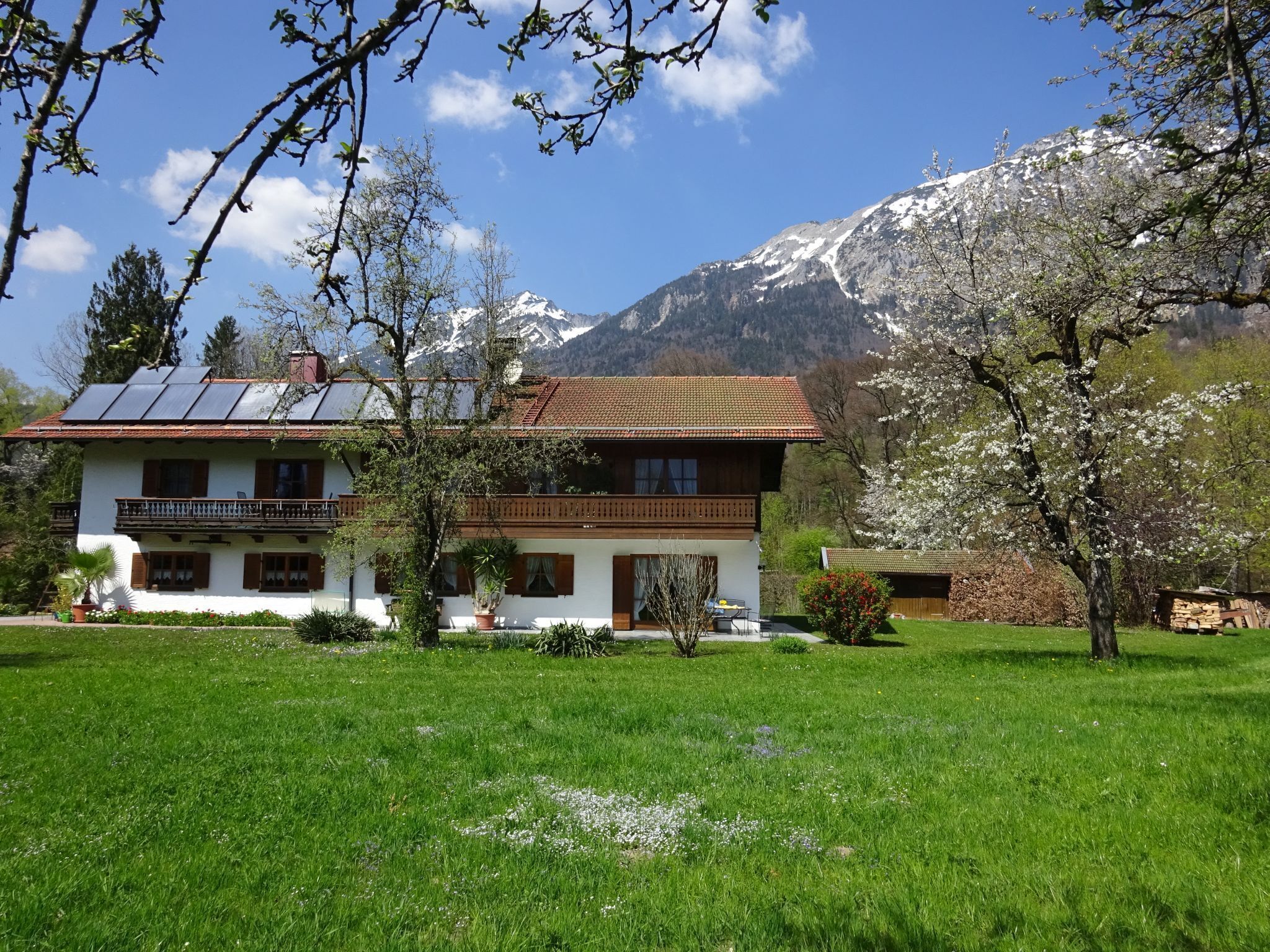 A two-story house with a balcony, surrounded by a green lawn and a mountain backdrop.