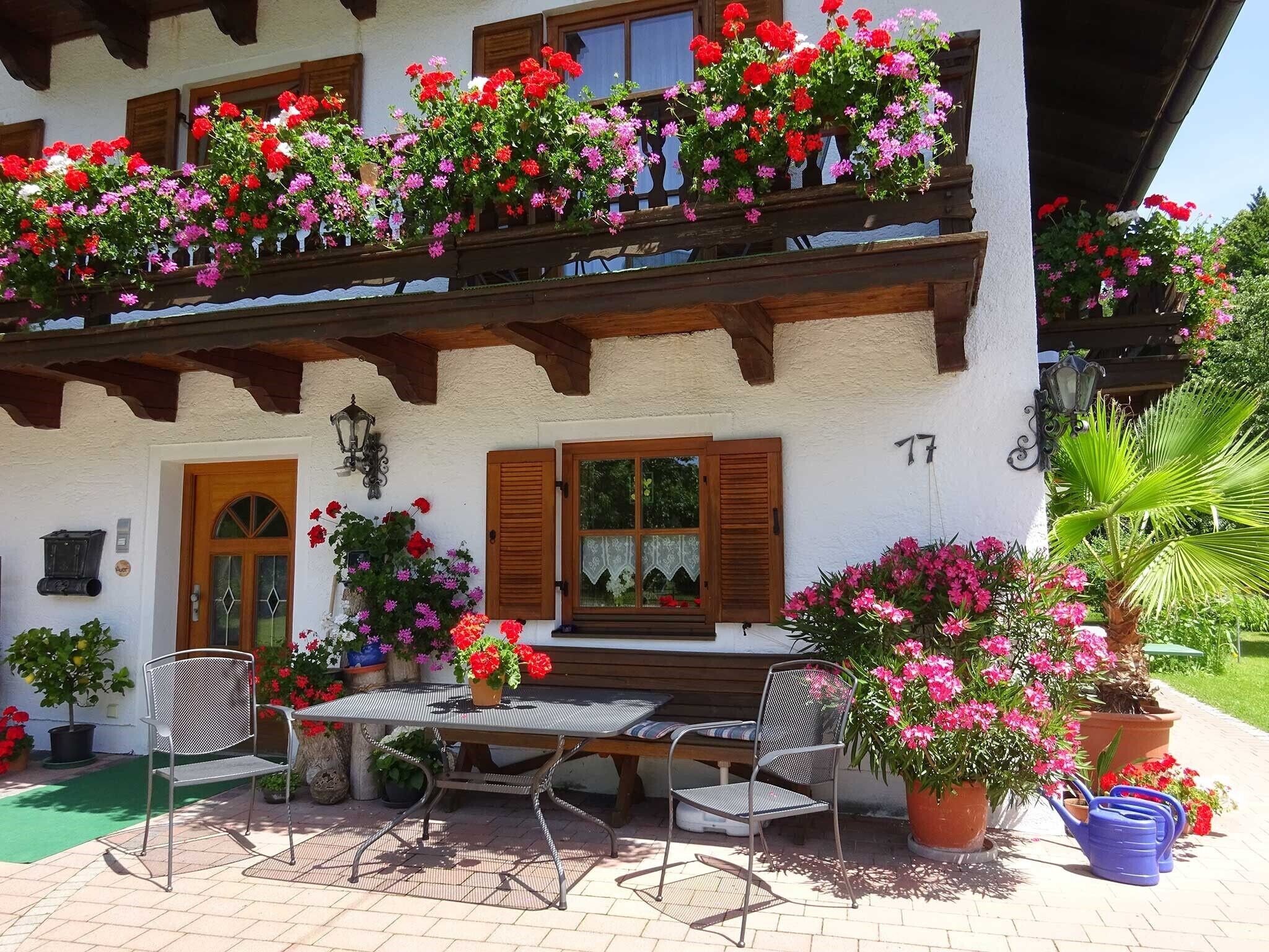 A two-story building with a balcony adorned with colorful flowers, a wooden door, and a table with chairs outside.