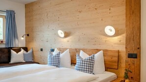 A double bed with white bedding and blue and white checkered pillows, a wooden headboard, and two wall-mounted lights. - Appartement "Hühnernest", 25 qm Obergeschoss, kombinierter Wohn- und Schlafraum (Höslwang)