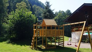 Une structure de jeu en bois comprenant une échelle, des balançoires et un petit bâtiment ressemblant à une maison.