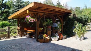 Un kiosque en bois avec un banc, entouré de plantes et de fleurs en pot.