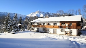 Un chalet à deux étages doté d’un balcon en bois, entouré d’arbres et de montagnes couverts de neige.