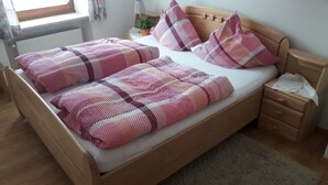 Ein hölzernes Bett mit einer pink-weiß karierten Tagesdecke und passenden Kissen, ein Nachttisch mit Lampe und ein kleiner Topfpflanze.