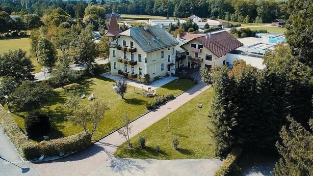 Ein großes, mehrstöckiges Gebäude im traditionellen Baustil, umgeben von üppiger Vegetation und Bergen im Hintergrund.