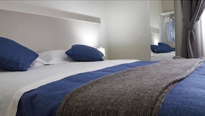 Une chambre d’hôtel avec un lit, des oreillers bleus, une couverture grise et une tête de lit blanche.
