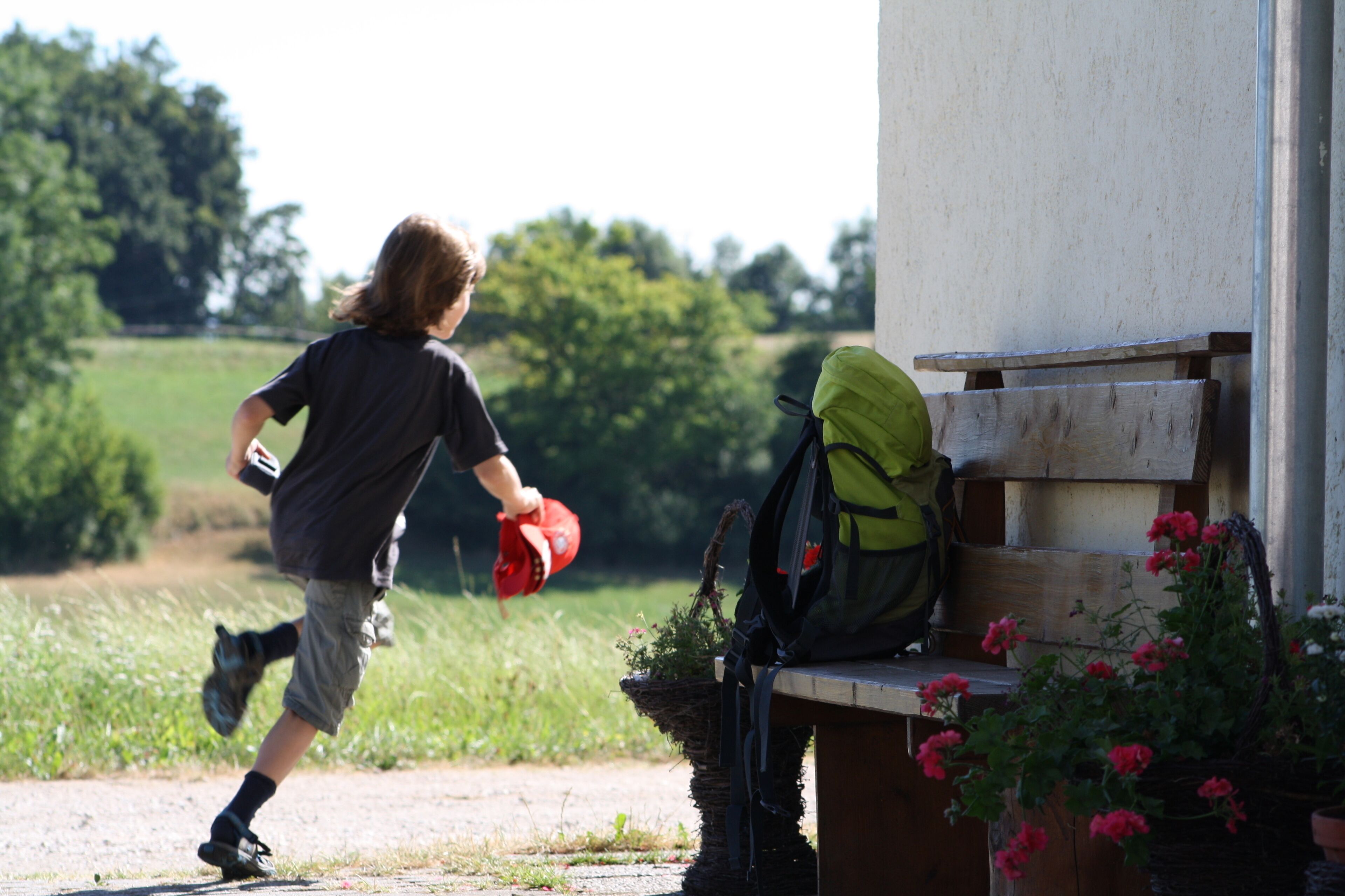 A person running towards a bench with a backpack and a red cap.