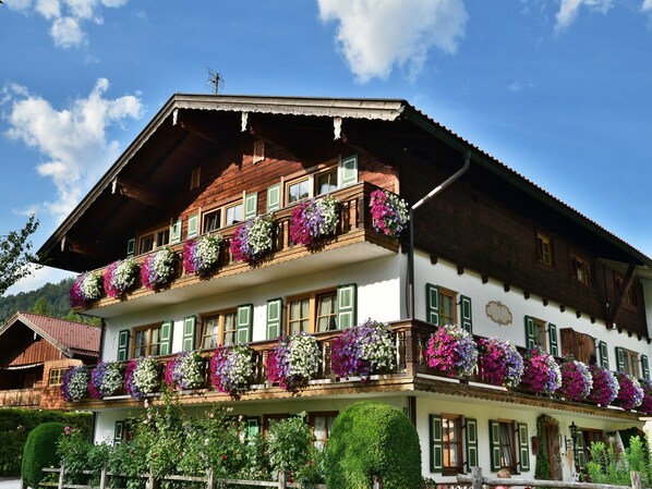A traditional multi-story building with balconies adorned with flowers, wooden architecture, and a clear sky.