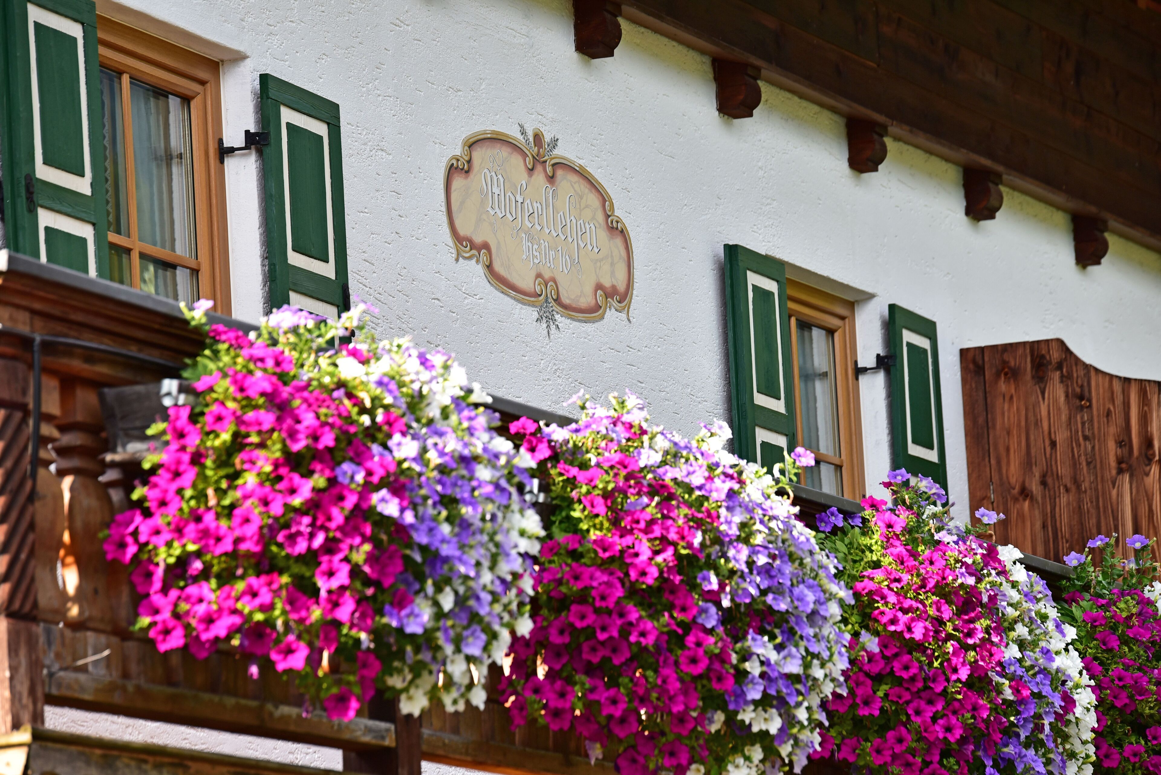 A building with a sign reading "Wolfelehen" and flower baskets on the balcony.